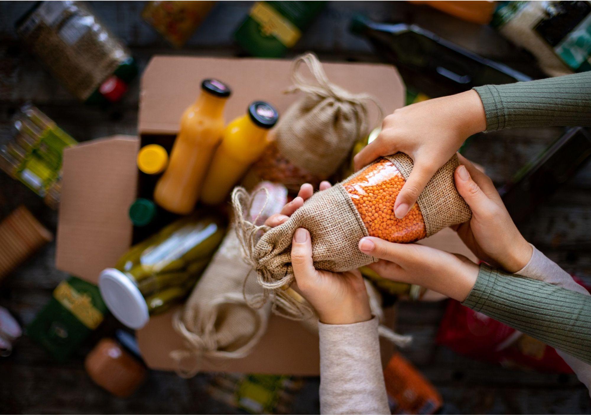 Two pairs of hands holding a bag of lentils with other jars and bags of food in the background