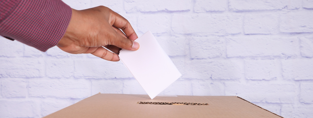 A hand holding an election vote hovering over a ballot box